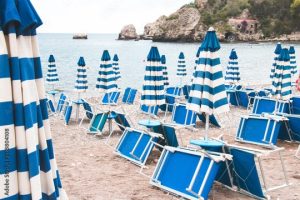 Blue sun umbrellas on a sandy beach with folded chaise lounges